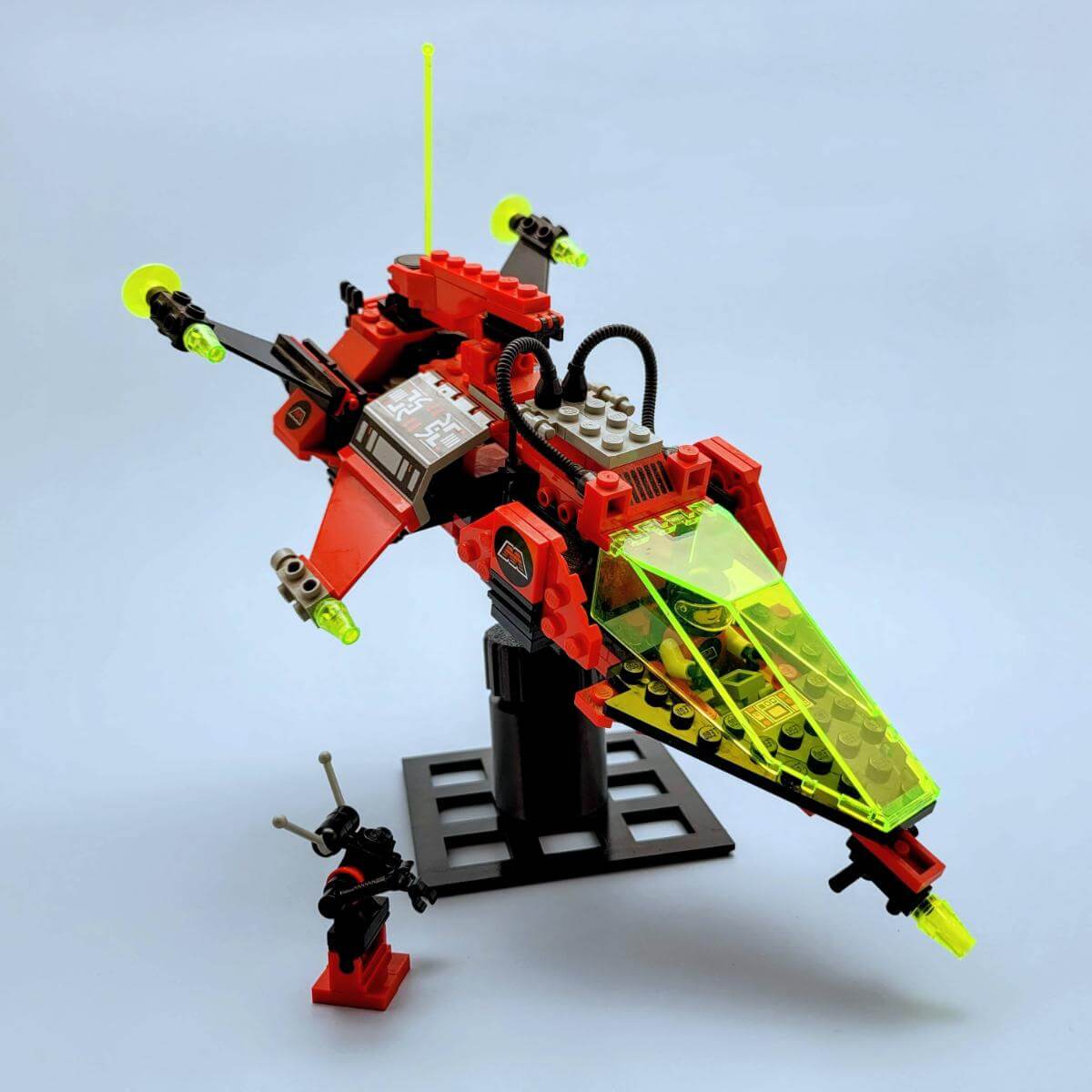 LEGO M-Tron spaceship posed mid-flight on a black tilt stand with included minifigure. Highlights the ship’s sleek angles and glowing neon parts. Ideal for vintage LEGO space collectors looking to elevate classic sets.