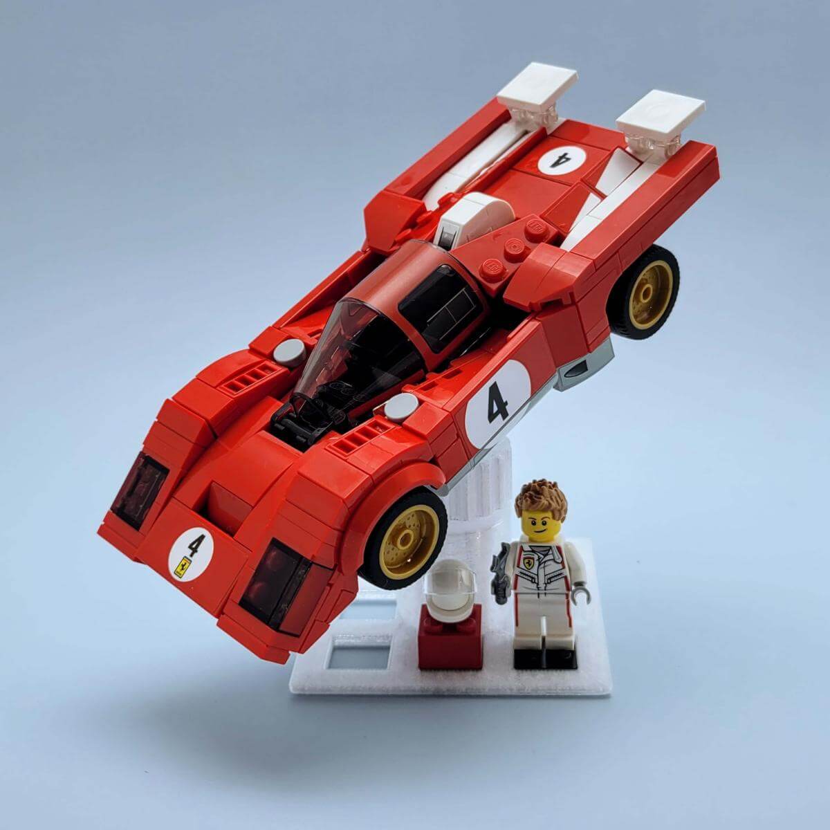 LEGO race car on a white tilt display stand, positioned mid-turn with matching driver minifigure beside it. Shows how to showcase vehicles in motion using a secure swivel mount. Perfect for collectors who want their speed builds angled on a shelf or inside a case.