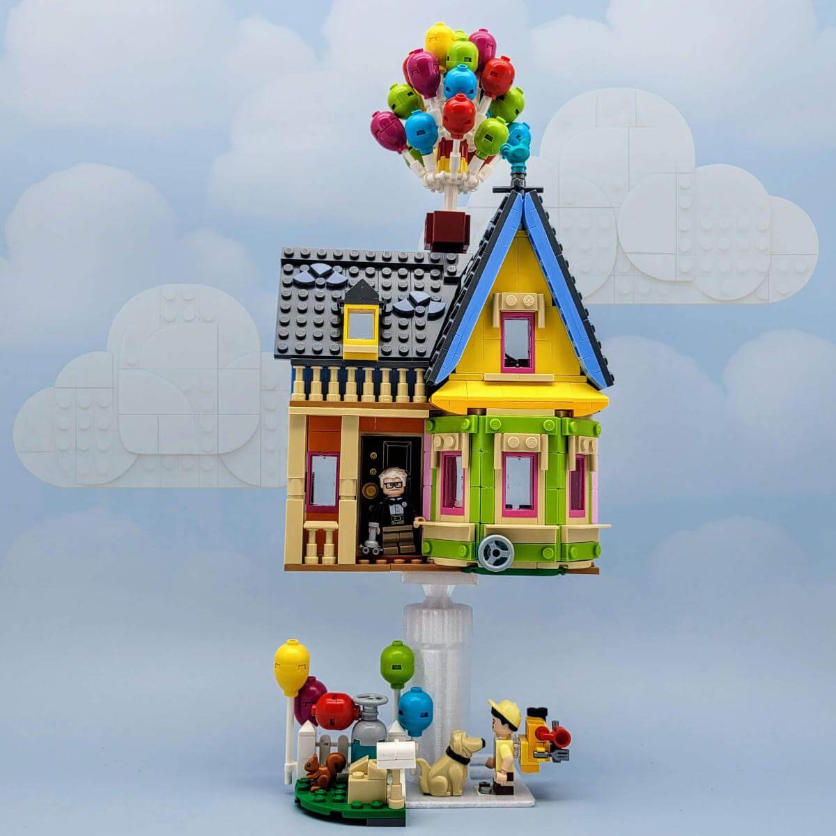 LEGO Up house display with colorful balloons floating in the sky, mounted on a custom white stand. Ideal for showcasing Pixar-themed LEGO sets with creative elevation and clean presentation. The stand gives the model a hovering effect, making it look like it's floating away just like in the movie. Perfect for fans of animation, unique LEGO builds, or decorative collector displays.