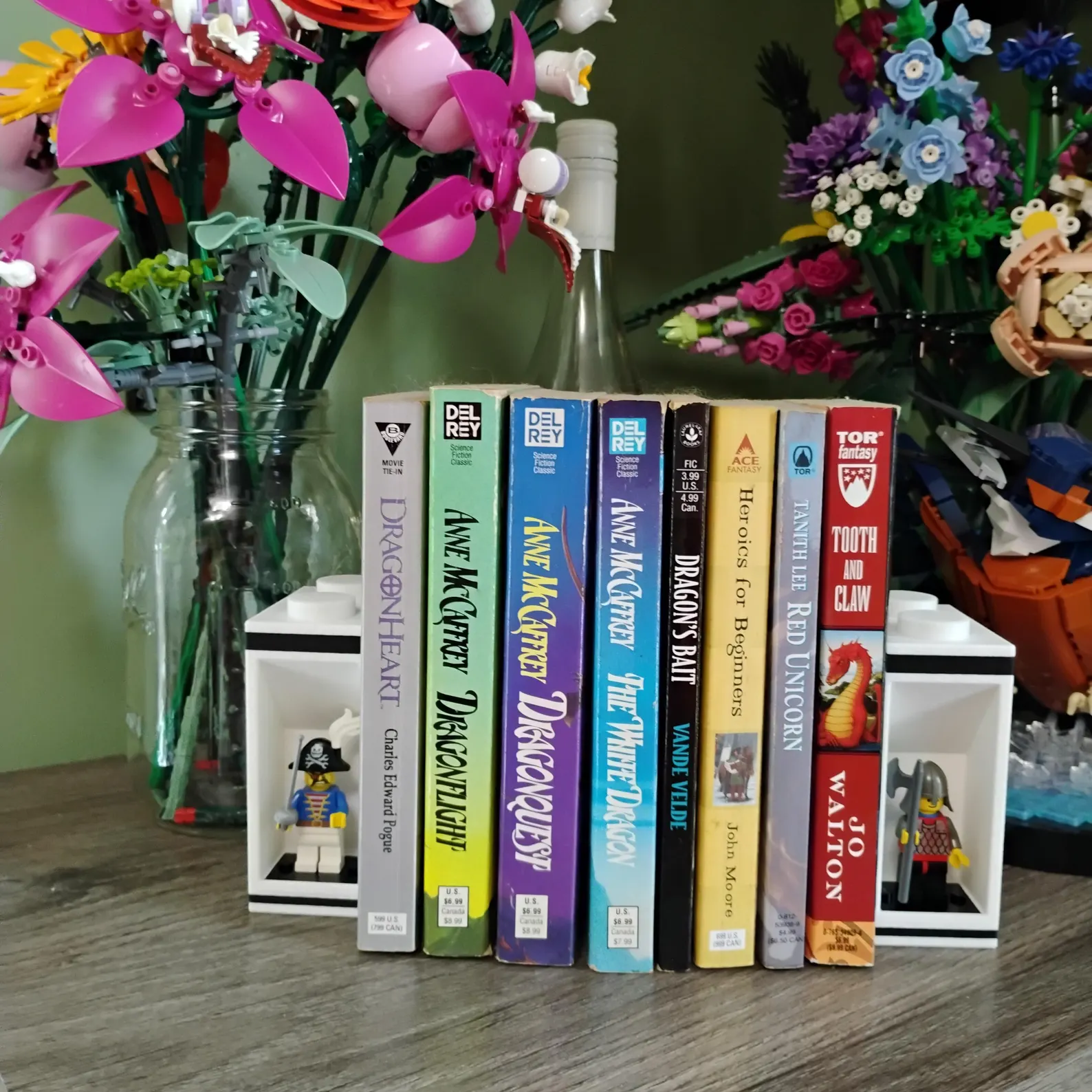 Colorful LEGO® minifigure bookends holding bright paperback books beside flowers. Functional shelf décor that merges display and utility.