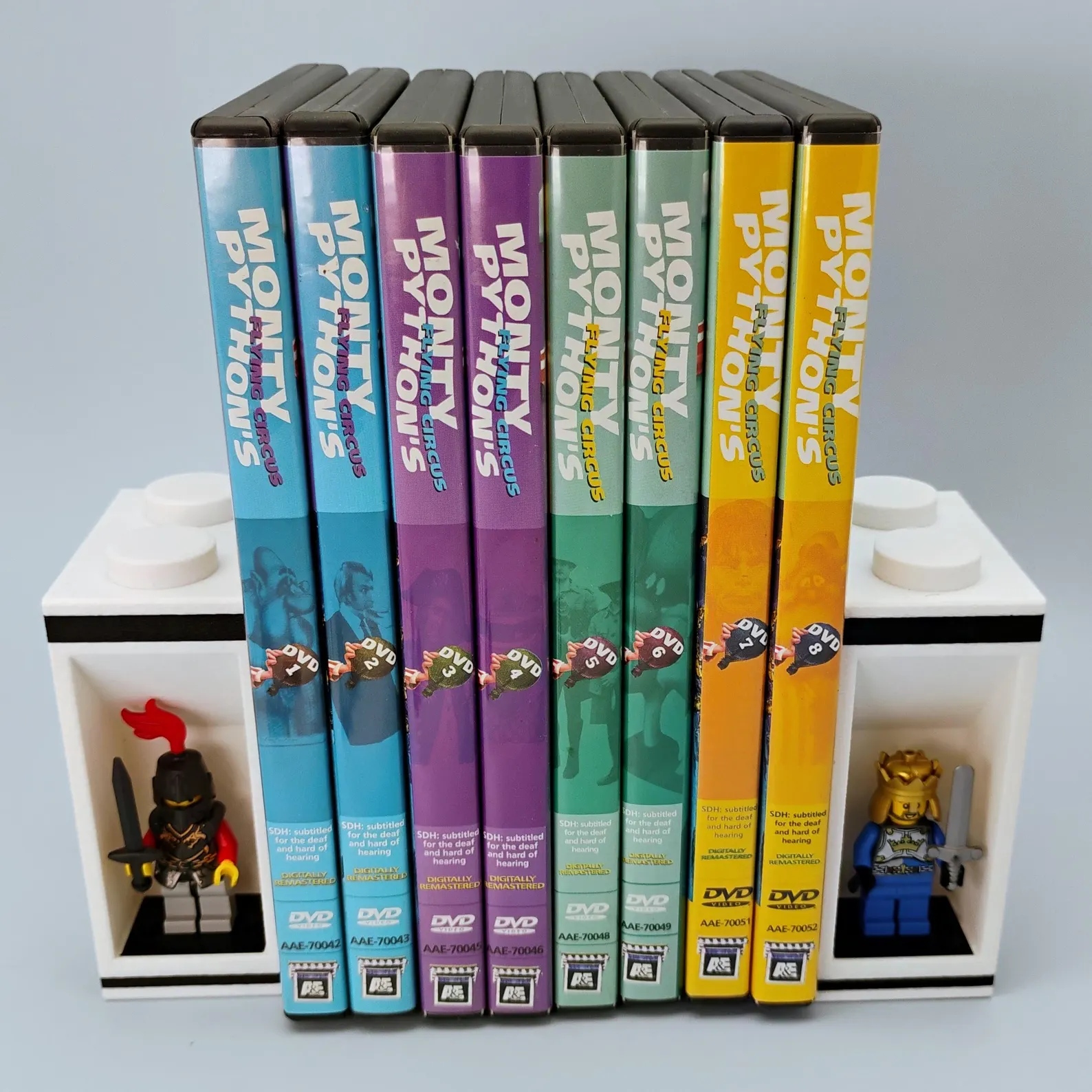 LEGO® minifigure bookends holding a colorful DVD collection. Modular bookend design includes integrated figure displays for collectible charm and shelf stability. Perfect for books or media collections.
