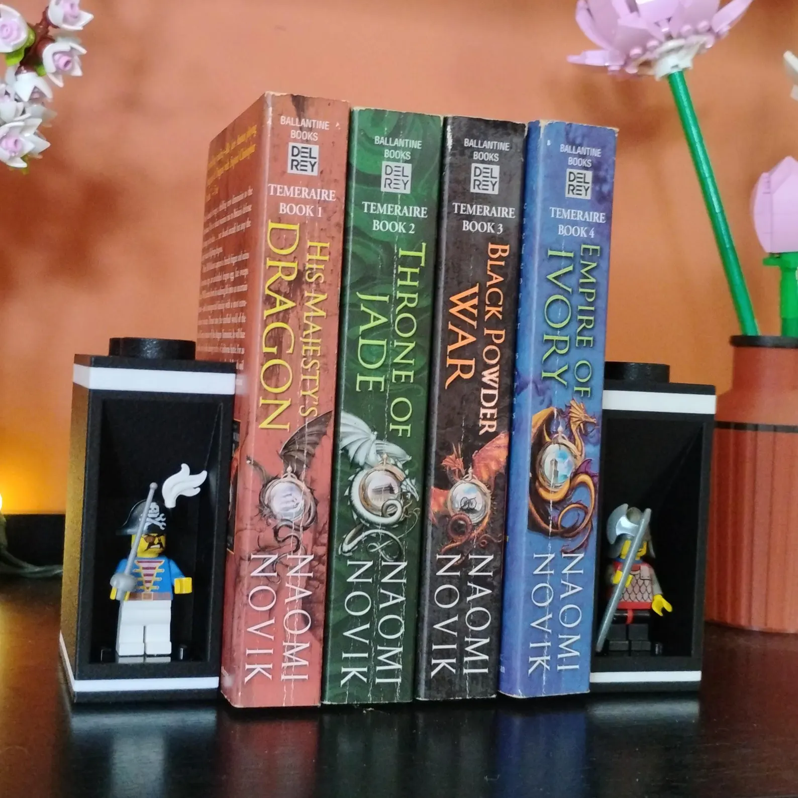 Fantasy novel set held by LEGO®-compatible bookends featuring minifigure display modules and decorative plants.