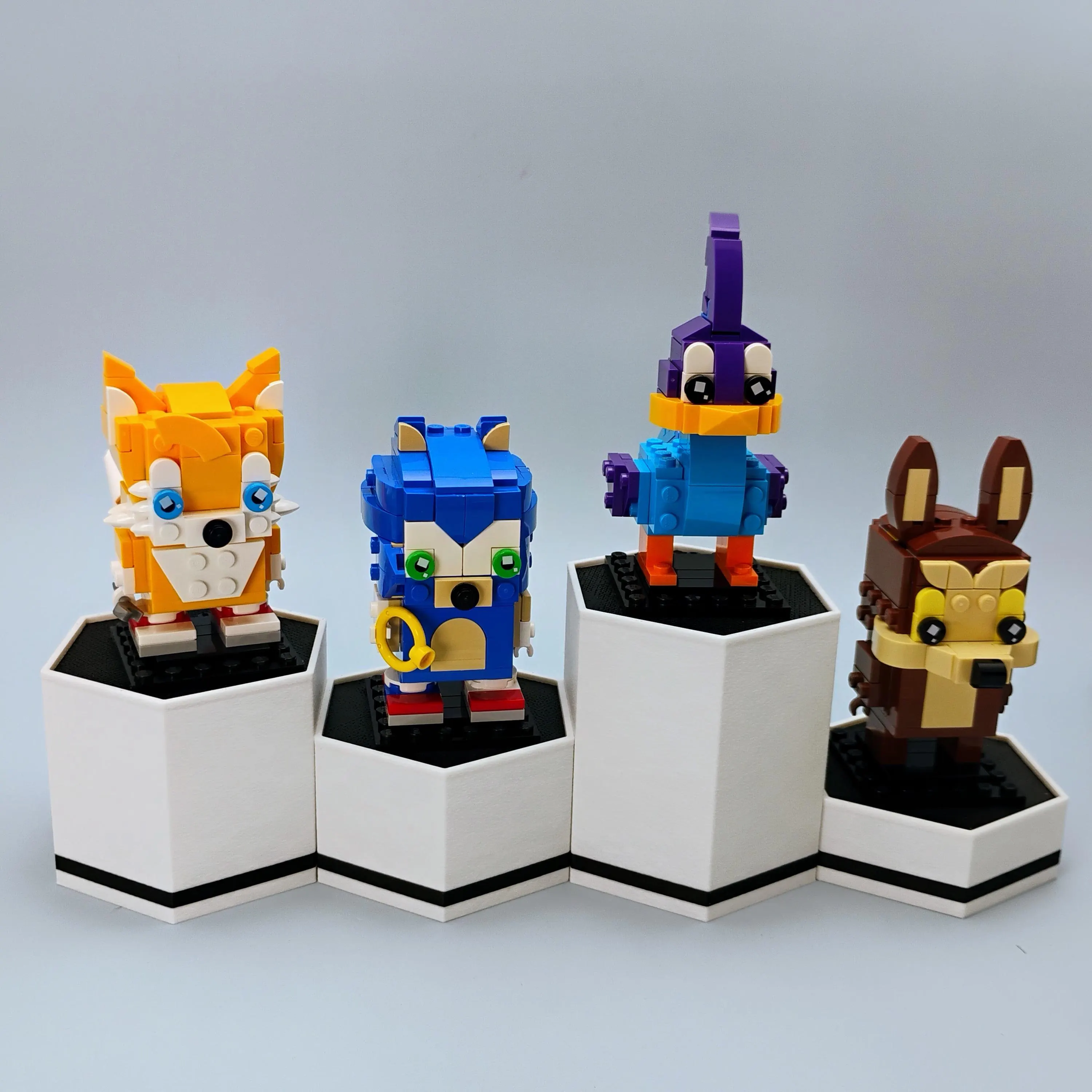 Pair of white hexagonal display stands for BrickHeadz and collectables arranged in minimalist layout.