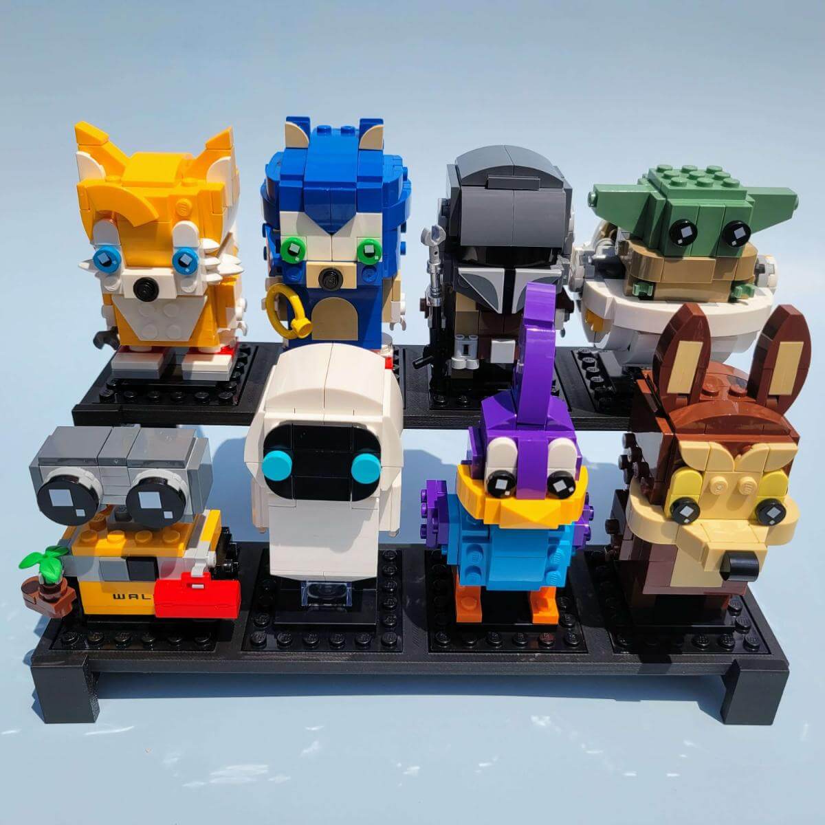 Front view of a two tier LEGO compatible display stand holding eight colorful BrickHeadz characters. The black plastic stand is designed for optimal visibility, with staggered rows to showcase each figure. Perfect for collectors who want a clean and compact way to display LEGO BrickHeadz on a shelf, desk, or display case. Sturdy and easy to assemble. Display stand only; figures not included.