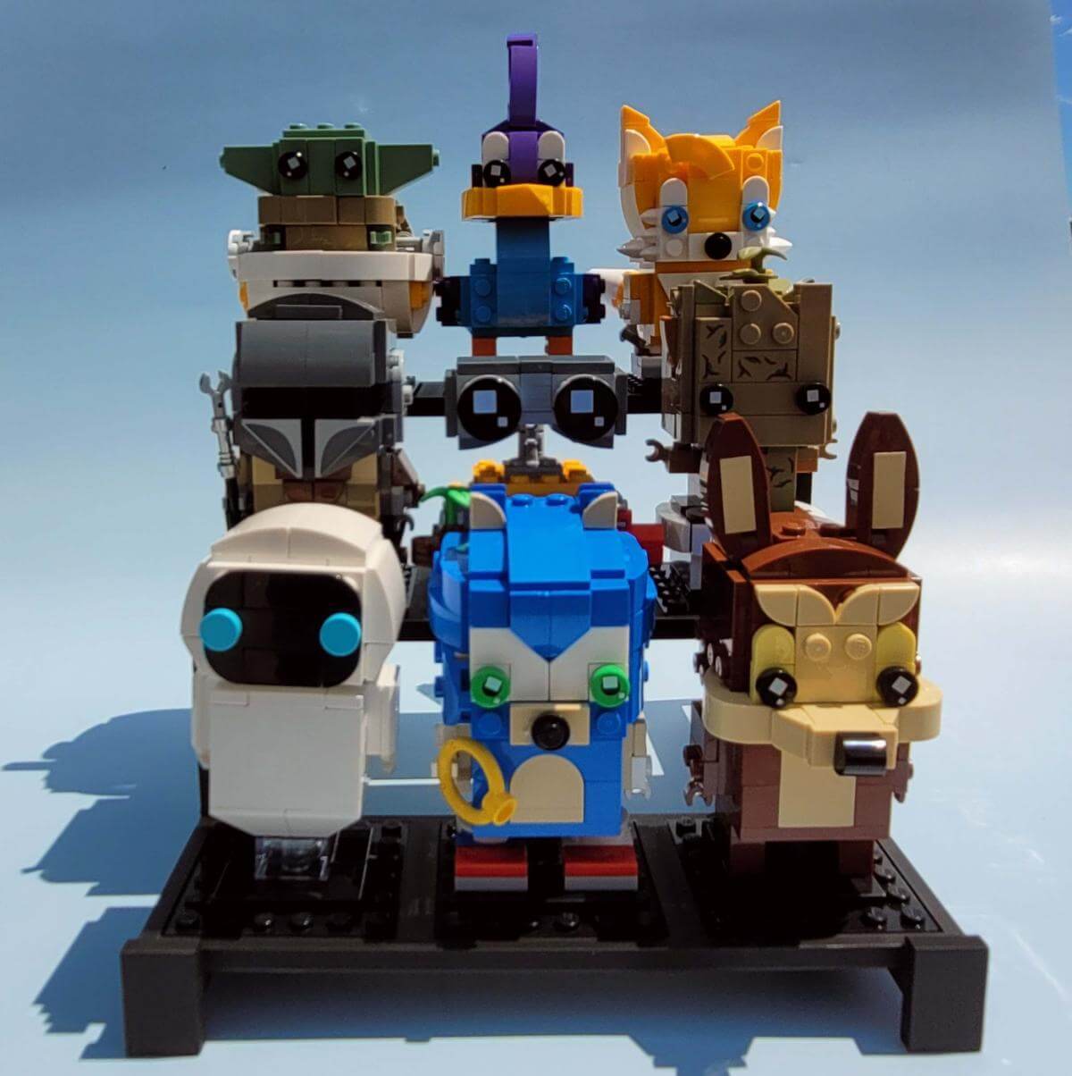 Three tier black LEGO compatible display stand holding nine colorful BrickHeadz in a staggered arrangement. Perfect for showcasing collectible figures. The stand raises each row for better visibility and organization. Ideal for shelves, desks, or LEGO fan displays. Display stand only; figures not included. Made of durable black plastic with smooth lines and clean finish.