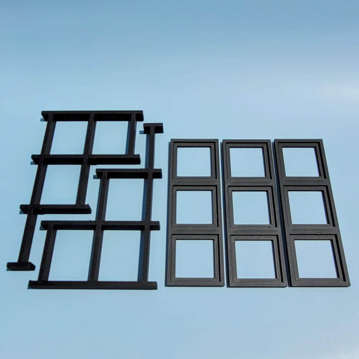 All components of the LEGO compatible BrickHeadz display stand laid flat on a blue background. The image shows each part prior to assembly, demonstrating compact shipping and easy setup. Pieces connect without tools, forming a sturdy three tier frame to hold nine BrickHeadz. Stand only.