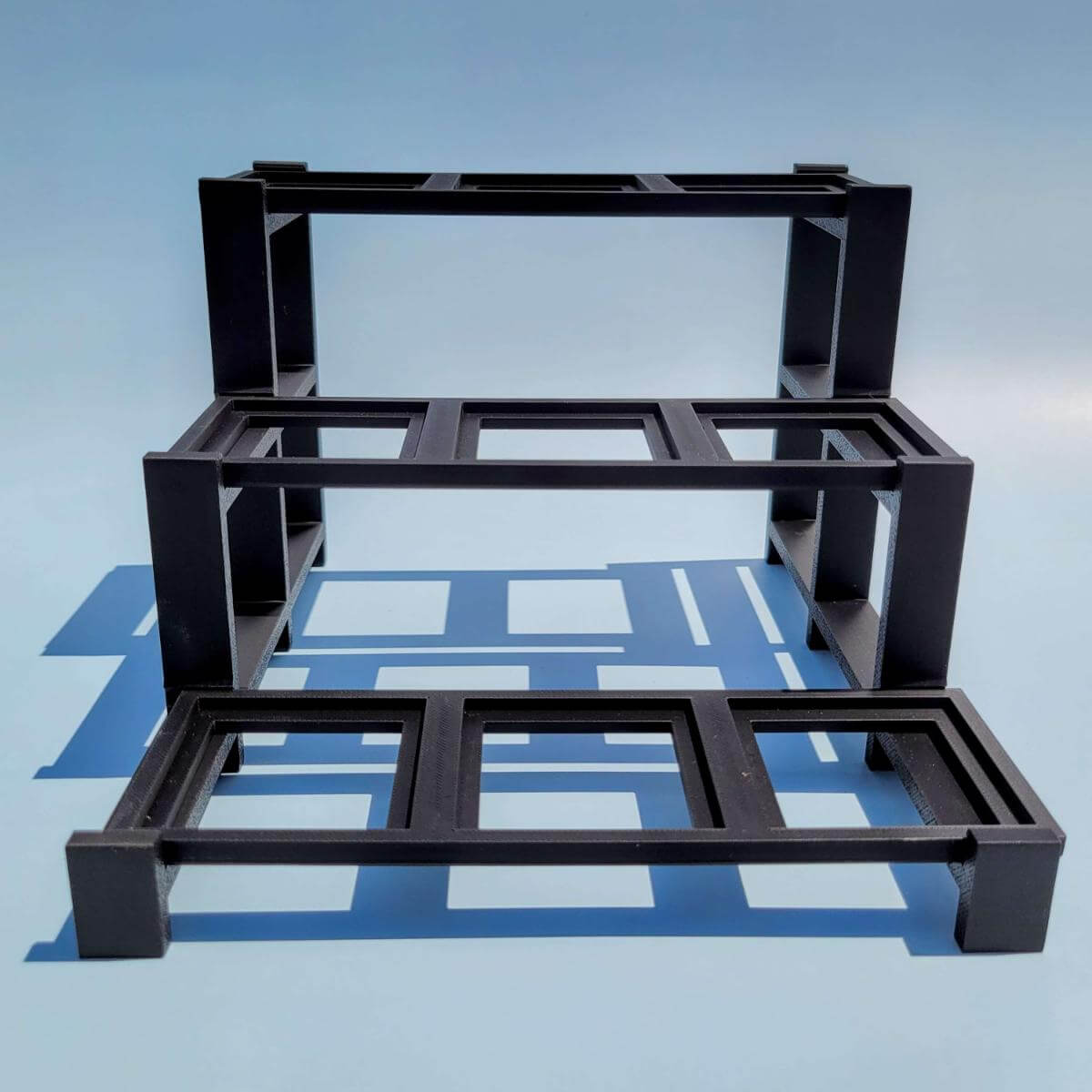 Front view of an empty black plastic LEGO compatible display stand. Designed with three raised tiers and nine slots to organize and display BrickHeadz. Clean, modern design for desks, shelves, or cabinets. Easy to assemble and disassemble. Compatible with standard LEGO BrickHeadz bases. Product shown is display stand only.