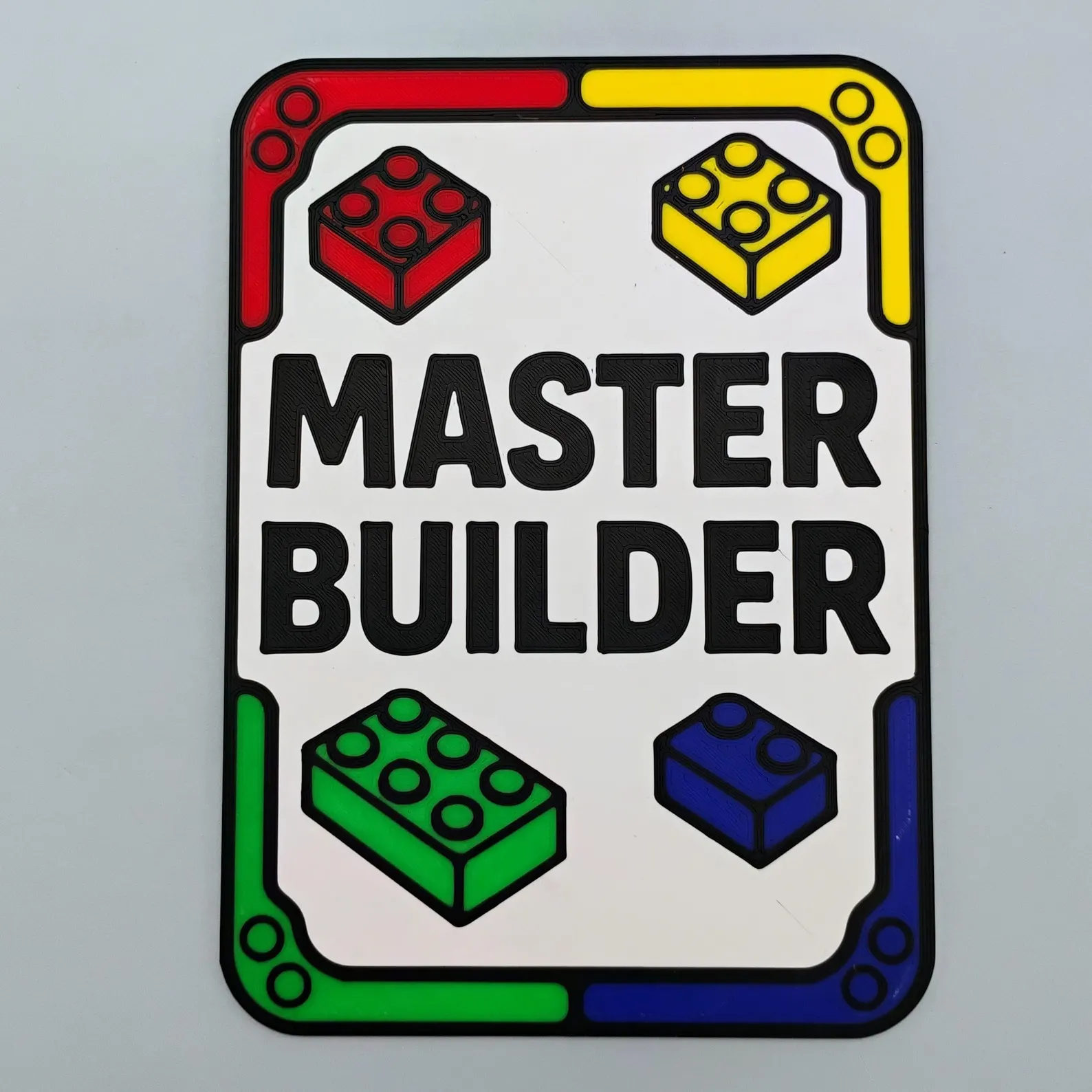 Flat lay photo of a 4 by 6 Master Builder sign showing the colorful brick-style border and centered text.