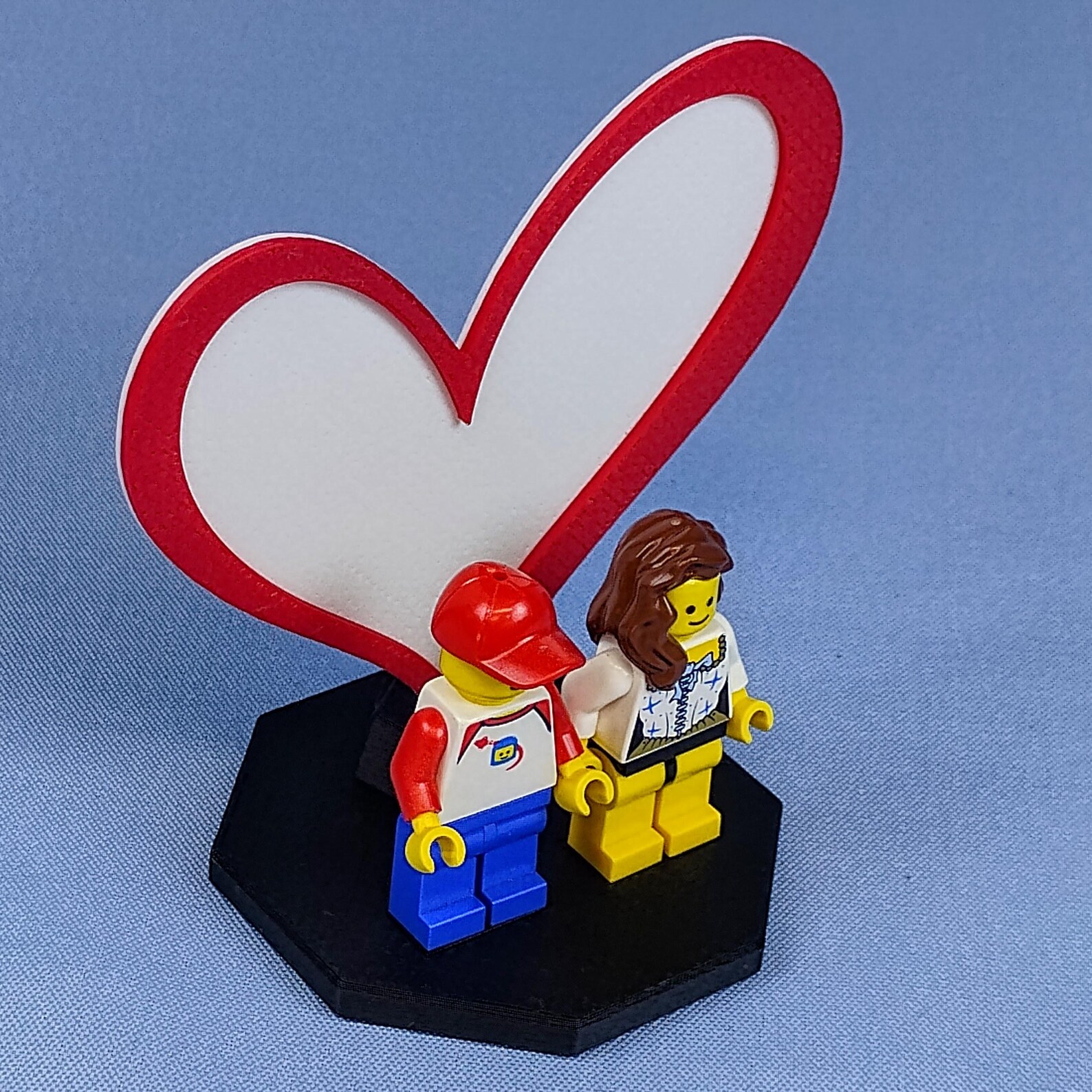 Angled view of the Heart Display for LEGO® minifigures showing the raised heart outline standing behind two figures, emphasizing depth, shadow, and the clean modern design.