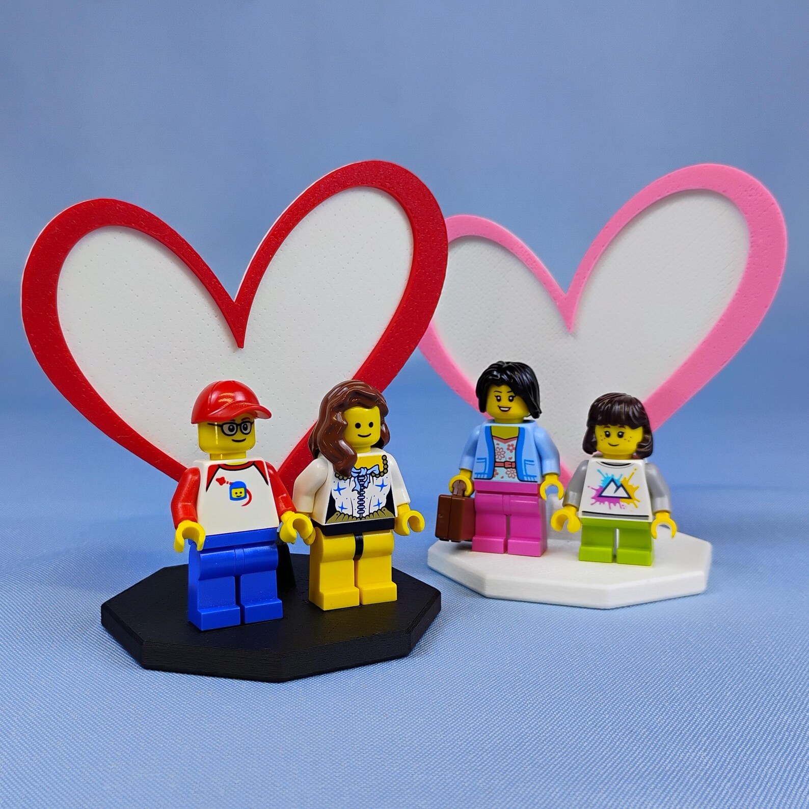 Two Heart Display stands shown side by side, each holding a pair of LEGO® minifigures, highlighting how the display works for couples, matching characters, or themed pairs.