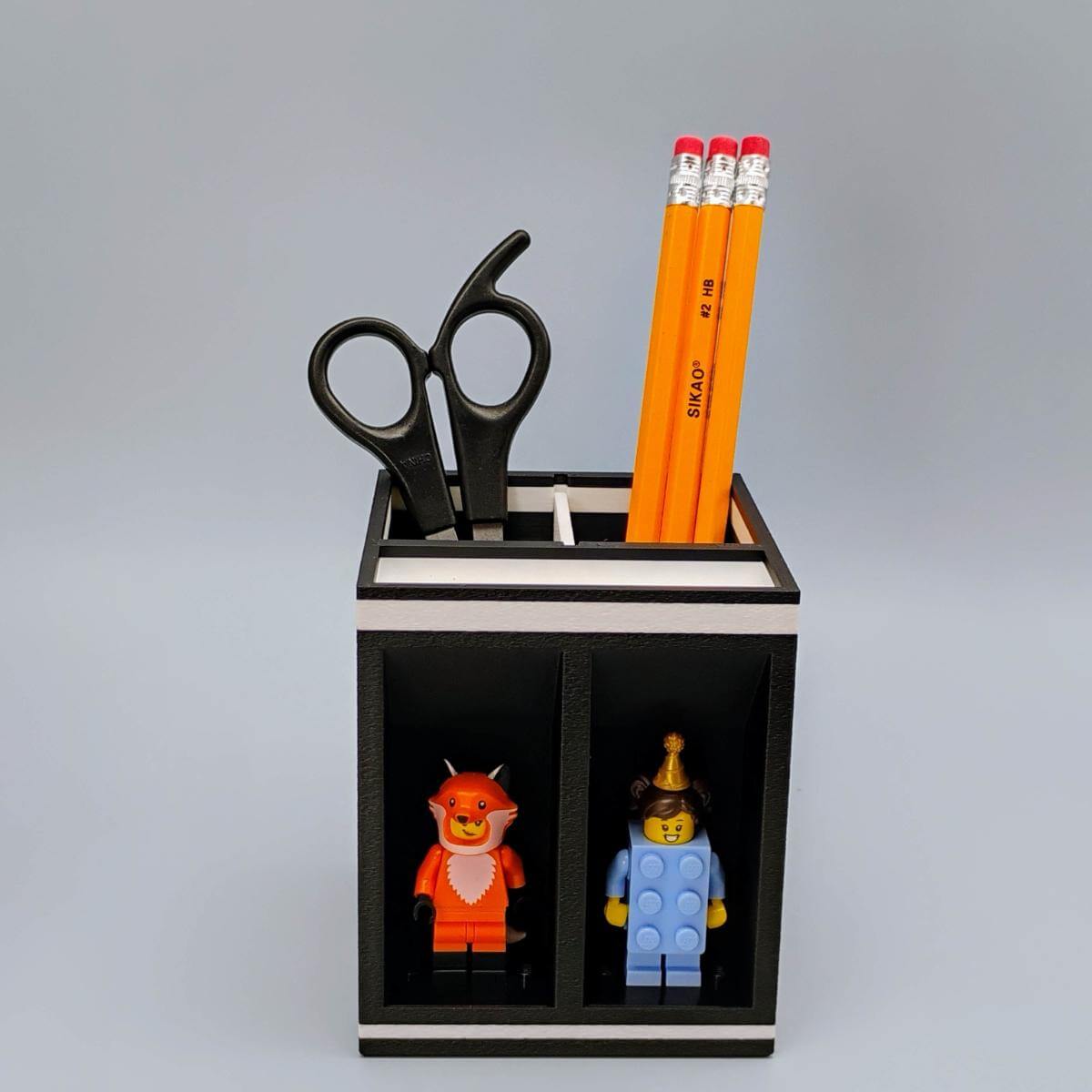 Compact LEGO minifigure desk organizer with two display slots, top tray, and customizable compartments for pens, pencils, or hobby tools. Great gift for LEGO fans or AFOLs who want a small workspace upgrade with room for creativity and character. Perfect for home office or maker spaces.