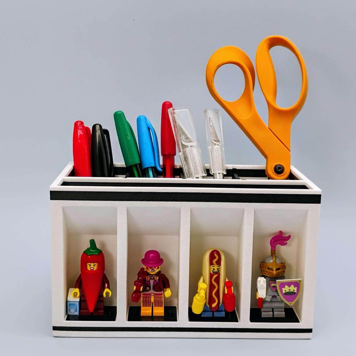 Standard-size LEGO-themed desk organizer with four minifig display slots and removable dividers. Holds scissors, pens, hobby knives, and more. A clever combination of desk utility and collectible figure display. Designed for adult LEGO fans, makers, artists, and creative workspaces.