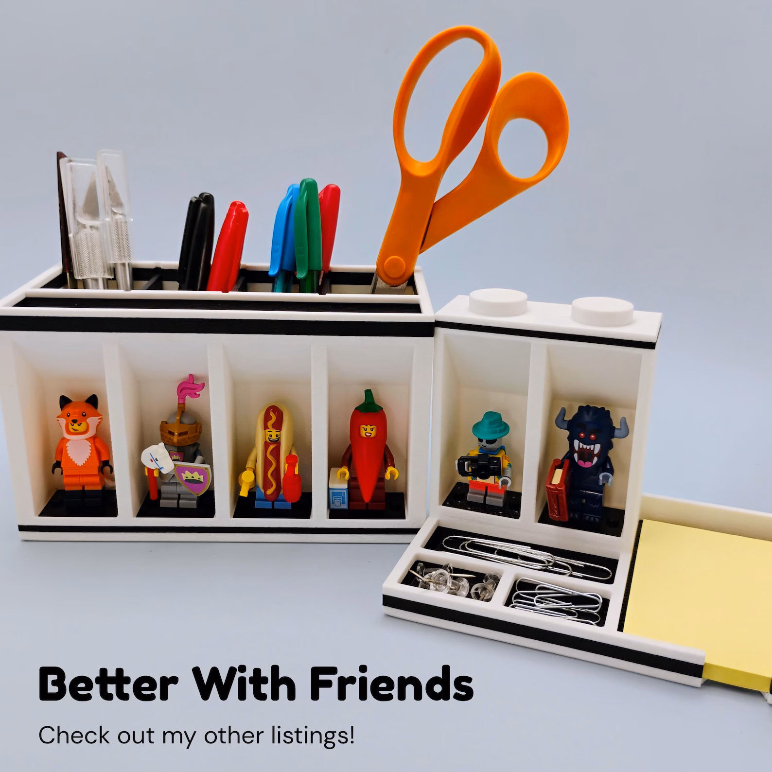 LEGO minifigure desk organizer shown in use with Post-it notes, pens, scissors, and displayed minifigures. Demonstrates how the organizer keeps everyday desk tools accessible while adding a playful display element to workspaces.