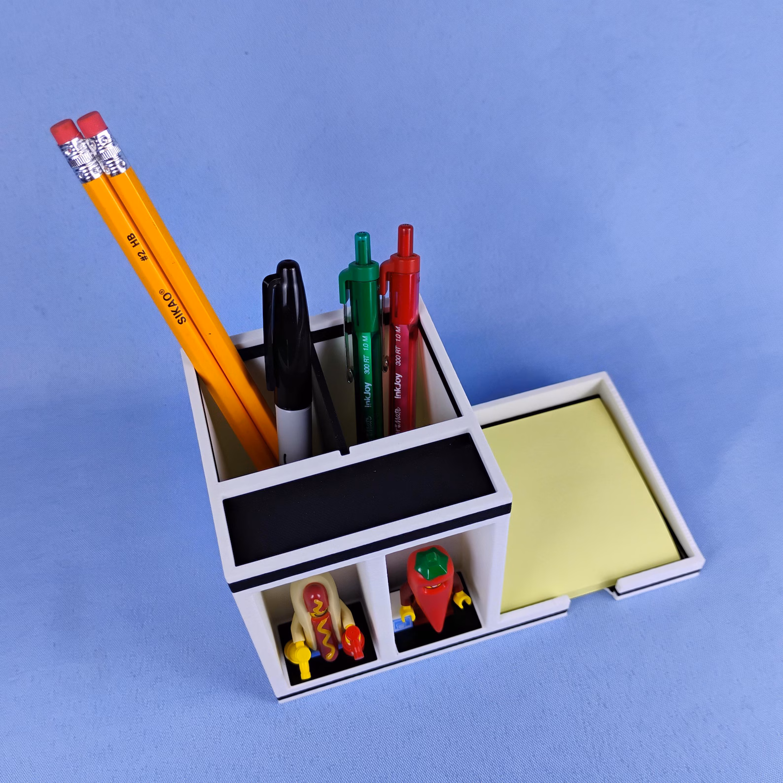 Angled view of a post-it note desk organizer highlighting the pen holder, sticky note tray, and display compartments. Shows depth, capacity, and layout from a three-quarter perspective.