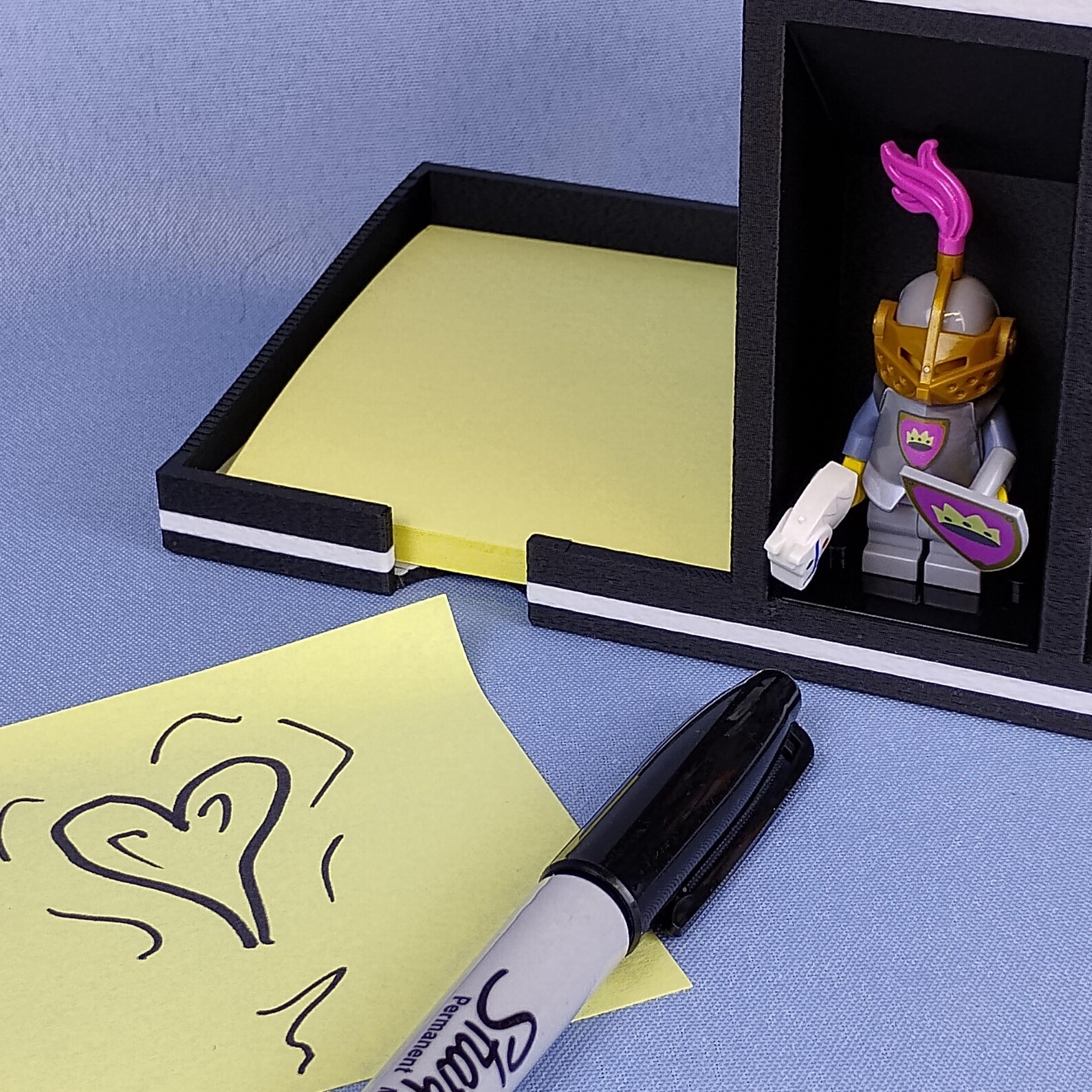 Flat lay view of a post-it note desk organizer on a home office workspace, showing sticky note storage, pen holder access, and display compartments arranged for everyday desk use.