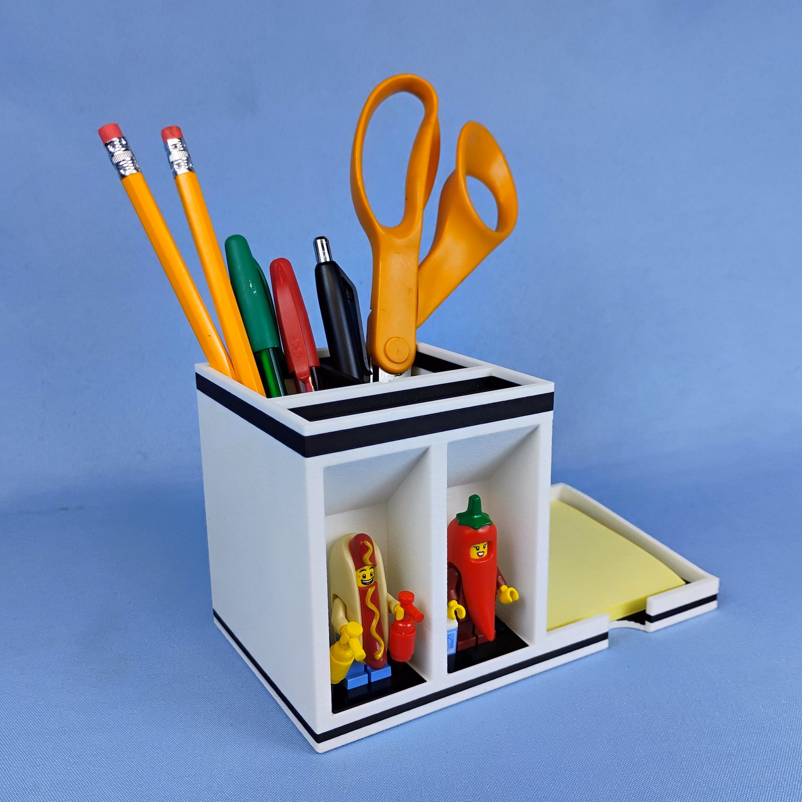 Post-it note desk organizer with pen and pencil caddy, featuring front-facing minifigure display shelves. Combines functional desk storage with a clean, modern display design.