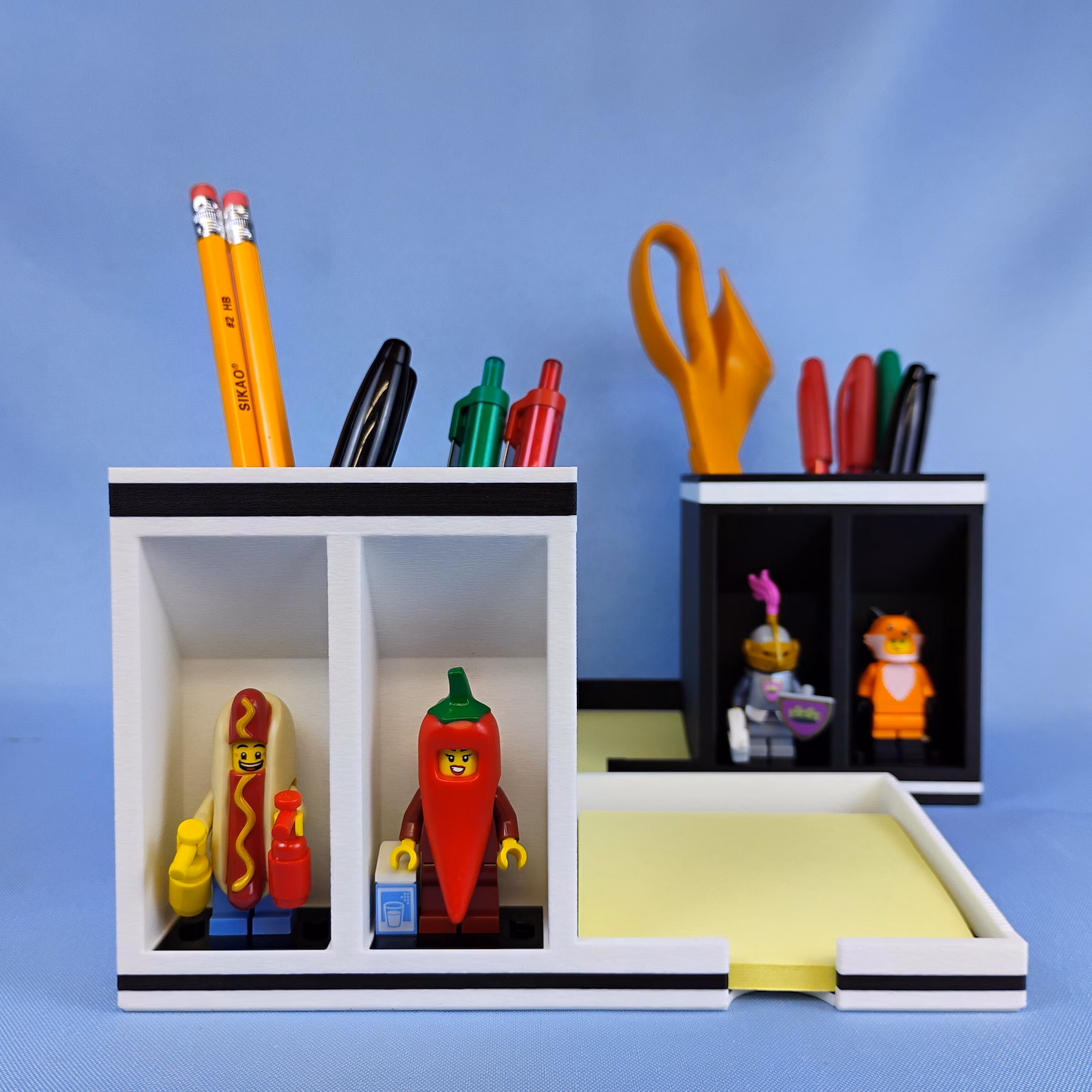 Post-it note desk organizer with pen and pencil holder, featuring front-facing display compartments for minifigures. Designed to keep sticky notes, writing tools, and small collectibles neatly organized on a home office desk.