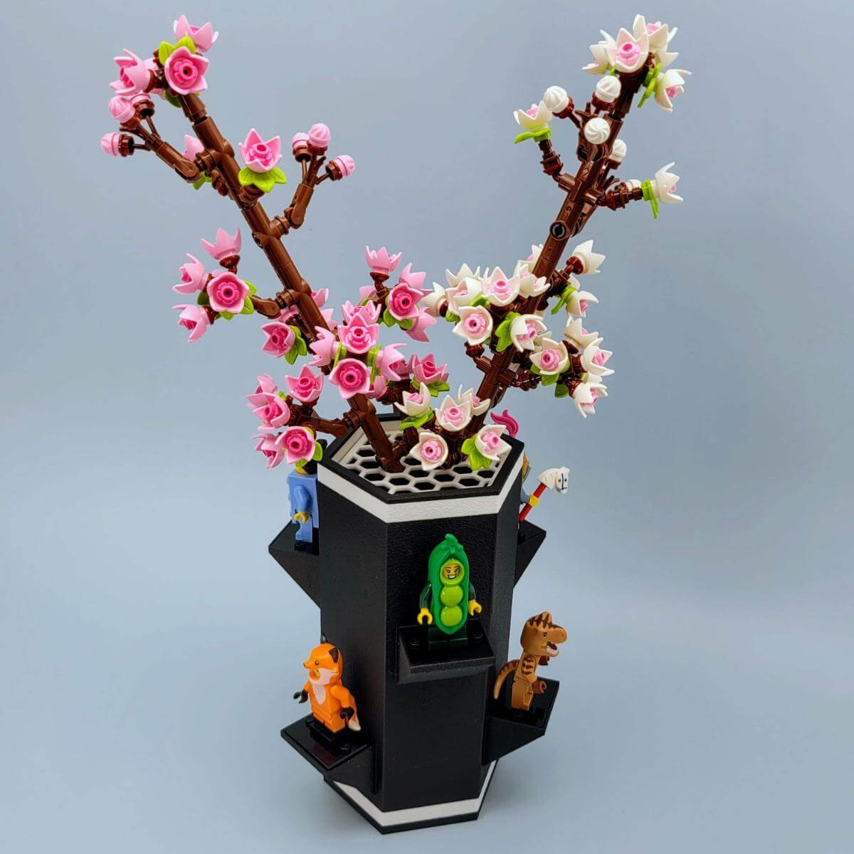 Top down angled view of a black LEGO compatible flower vase featuring a honeycomb style internal grid to support LEGO cherry blossom stems. Minifigures are visible on each platform around the vase. Highlights vase construction and floral support functionality.