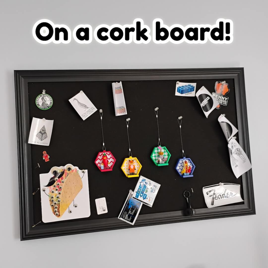 Hexagon LEGO® minifigure displays hung from pushpins on a cork board near notes and photos. Easy office or dorm gallery with compact footprint.