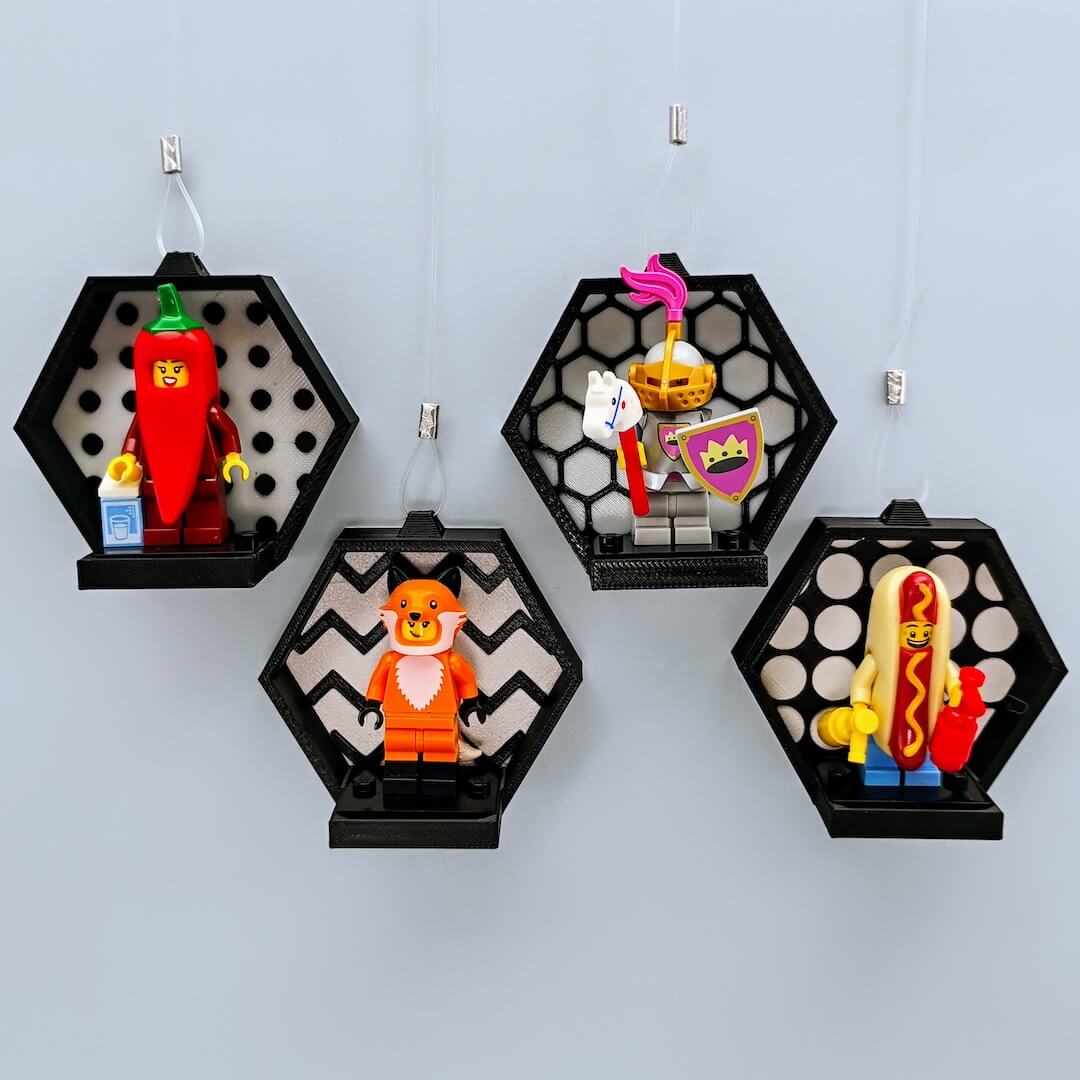 Five black hexagon LEGO® minifigure displays on a pale blue wall, showing studs, hexagons, zig-zags, and circles face patterns for a clean gallery look. Mix and match colors and patterns.