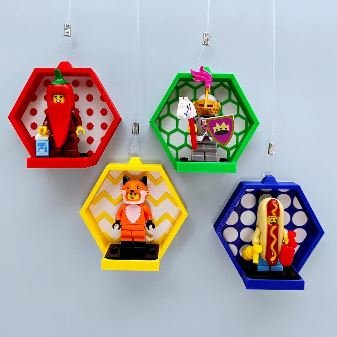 Four hexagon hanging LEGO® minifigure displays on a light gray wall, colorful frames with patterned faces, arranged as a modular honeycomb for kids rooms and collector spaces. Renter friendly window display option with suction hooks available.
